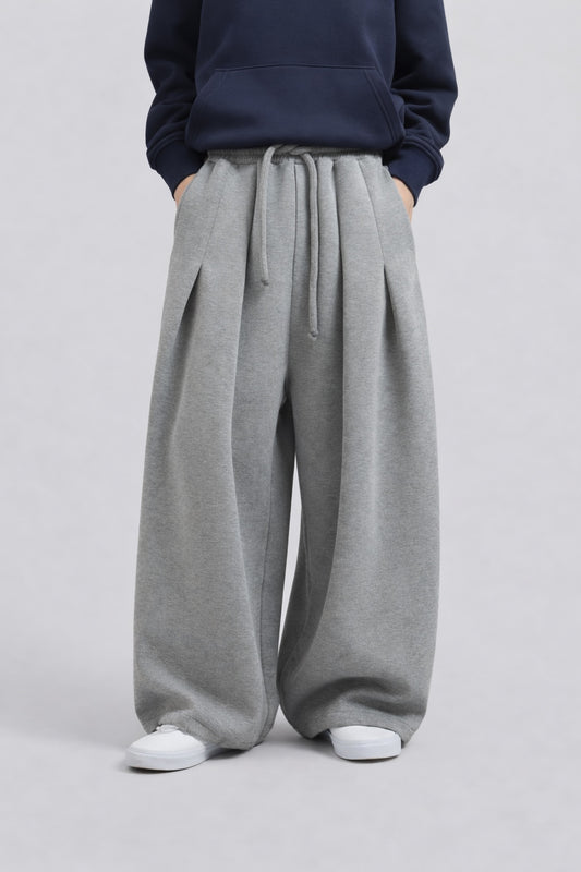 A person wearing wide-leg gray sweatpants with a drawstring waist, paired with a navy hoodie and white sneakers, shown from the chest down against a light gray studio background.