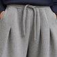 Close-up of a person wearing heather gray pleated sweatpants with a matching drawstring waist, paired with a navy hoodie.
